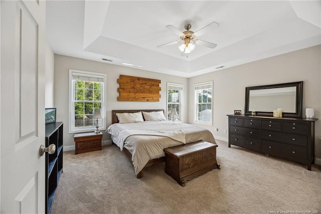 bedroom featuring a tray ceiling, light carpet, baseboards, and a ceiling fan