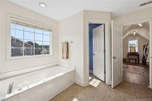 full bath featuring a garden tub, baseboards, lofted ceiling, and tile patterned flooring