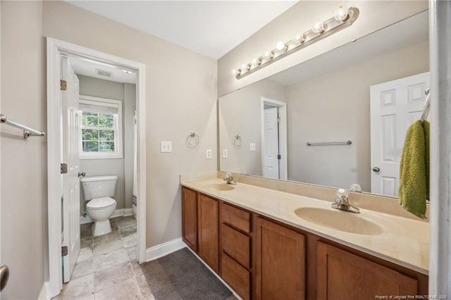 bathroom with toilet, double vanity, and baseboards