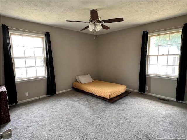 carpeted bedroom with multiple windows, baseboards, ceiling fan, and a textured ceiling