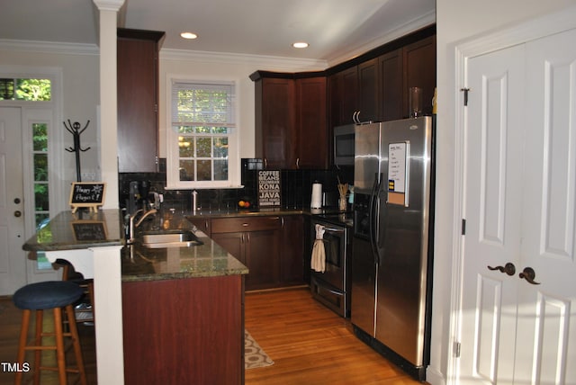 kitchen with stainless steel appliances, a sink, a breakfast bar area, light wood finished floors, and decorative backsplash