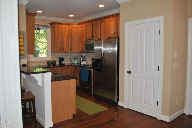 kitchen with stainless steel appliances, a peninsula, dark countertops, brown cabinetry, and dark wood-type flooring
