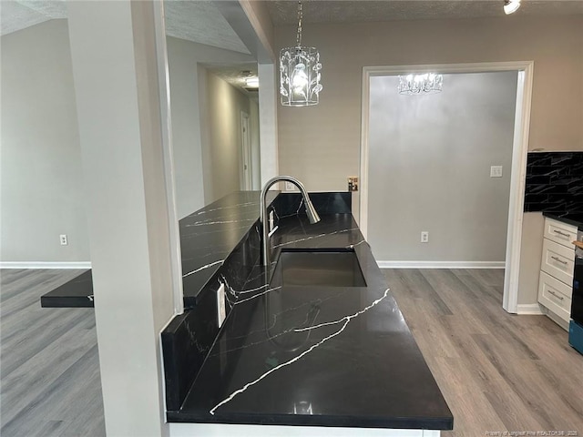 kitchen featuring dark countertops, wood finished floors, a chandelier, white cabinetry, and baseboards