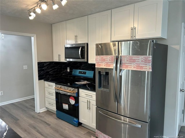 kitchen with appliances with stainless steel finishes, white cabinetry, light wood-style floors, backsplash, and dark countertops