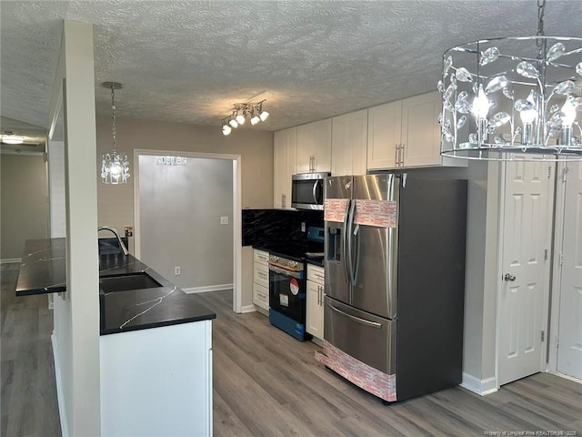 kitchen with stainless steel appliances, wood finished floors, dark countertops, white cabinets, and a textured ceiling