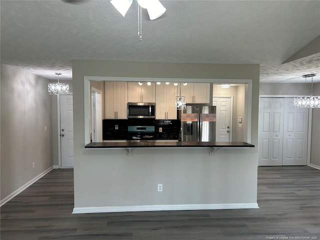 kitchen featuring appliances with stainless steel finishes, a chandelier, baseboards, dark countertops, and a textured ceiling