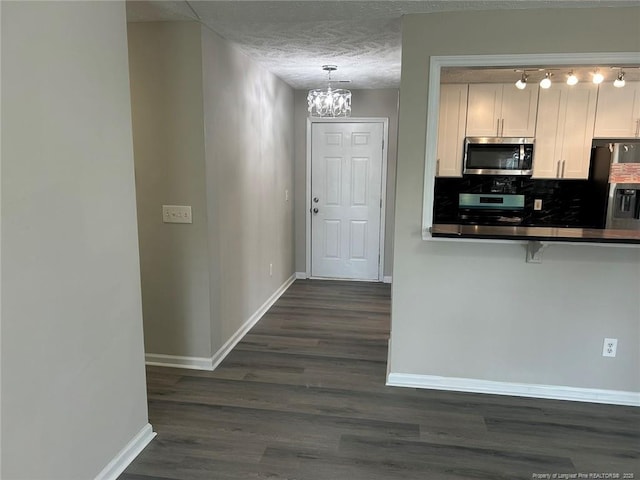 kitchen with stainless steel appliances, baseboards, dark countertops, a chandelier, and dark wood finished floors