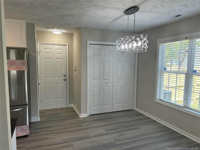 unfurnished dining area with dark wood-type flooring, a textured ceiling, baseboards, and a chandelier