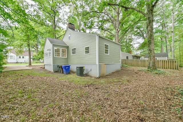 rear view of house with a chimney, fence, and cooling unit