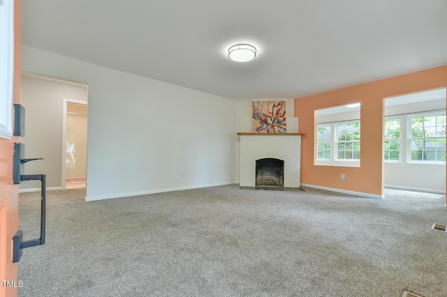 unfurnished living room featuring carpet, a fireplace with flush hearth, and baseboards