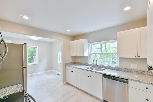 kitchen featuring appliances with stainless steel finishes, a sink, white cabinets, light stone countertops, and baseboards