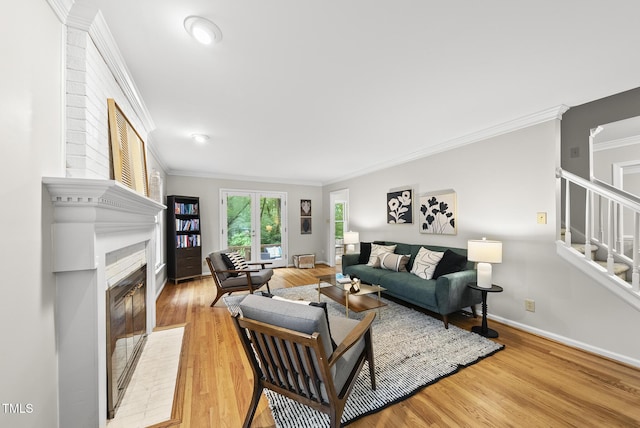 living area with ornamental molding, light wood-style floors, stairs, a fireplace with flush hearth, and baseboards