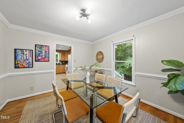 dining area featuring light wood-style flooring, crown molding, and baseboards