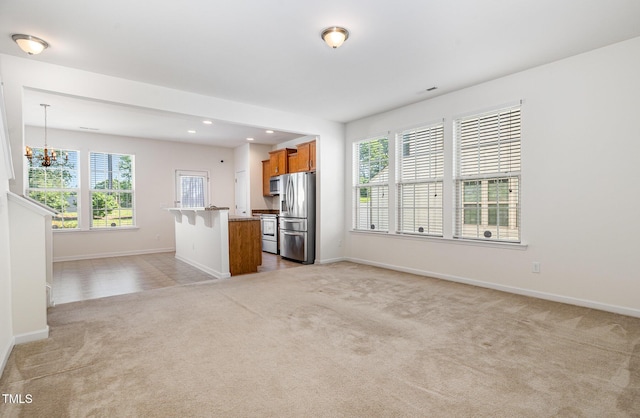 unfurnished living room with light carpet, plenty of natural light, a chandelier, baseboards, and recessed lighting