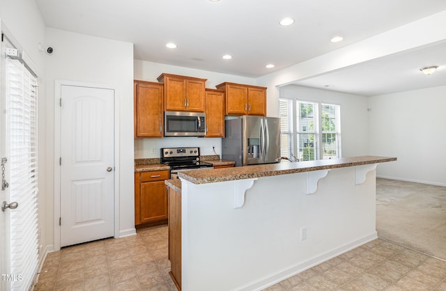 kitchen with stainless steel appliances, a kitchen bar, brown cabinetry, recessed lighting, and a center island with sink