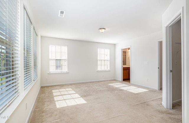unfurnished bedroom featuring light colored carpet, ensuite bath, and baseboards