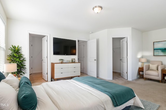 bedroom with a walk in closet, baseboards, a closet, and light carpet