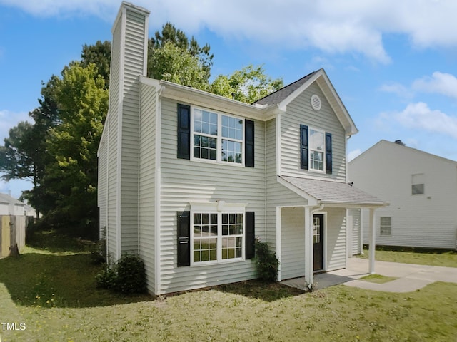 view of front of house with a chimney, roof with shingles, a front yard, and a patio area