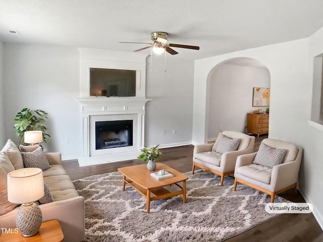 living area featuring a ceiling fan, arched walkways, wood finished floors, and baseboards