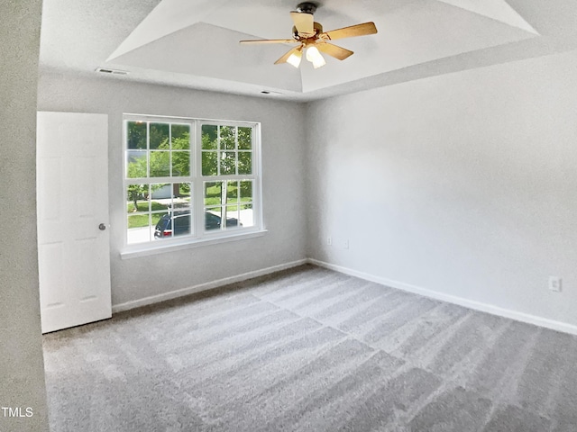 carpeted empty room with a ceiling fan, a tray ceiling, and baseboards