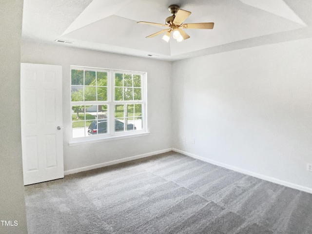 empty room with ceiling fan, a raised ceiling, carpet floors, and baseboards