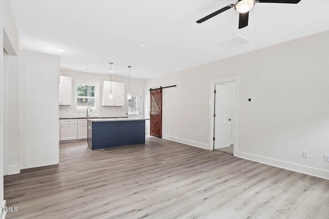 kitchen featuring a barn door, white cabinetry, a ceiling fan, light wood finished floors, and a center island