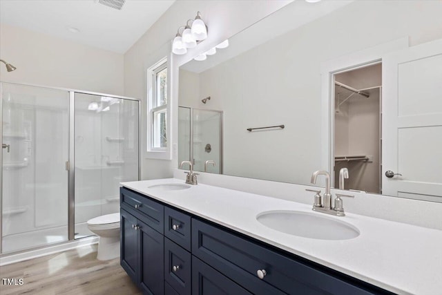 bathroom featuring a stall shower, double vanity, wood finished floors, toilet, and a spacious closet