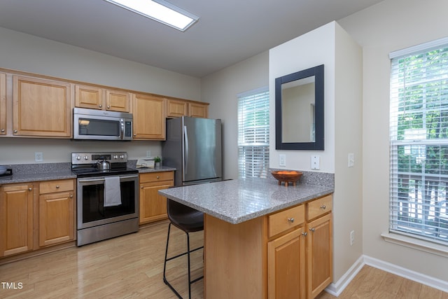 7244 Galon Glen Rd, Raleigh, NC 27613 - kitchen with appliances with stainless steel finishes, light wood finished floors, a kitchen bar, stone countertops, and a peninsula