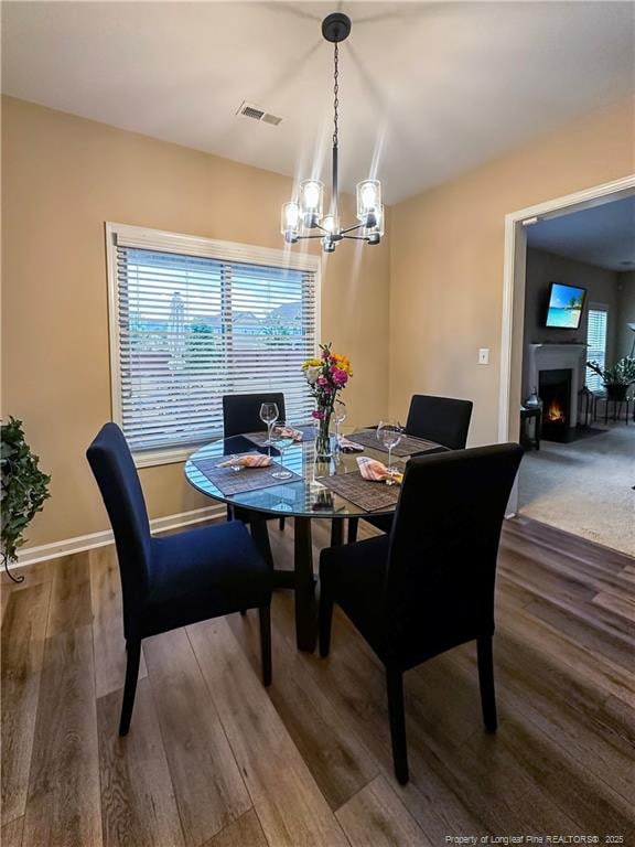 196 Wedgefield Dr, Raeford, NC 28376 - dining area featuring wood finished floors, a chandelier, a lit fireplace, and baseboards