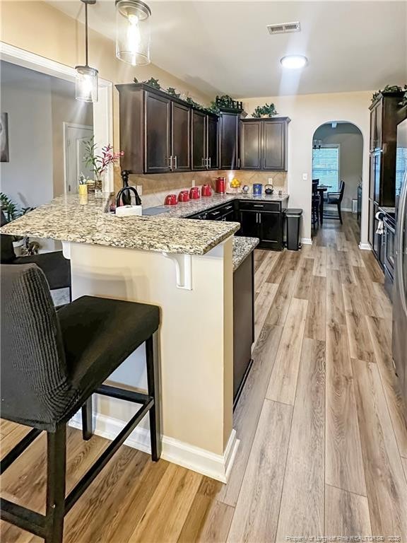 196 Wedgefield Dr, Raeford, NC 28376 - kitchen with arched walkways, a peninsula, light stone countertops, light wood-type flooring, and a breakfast bar area