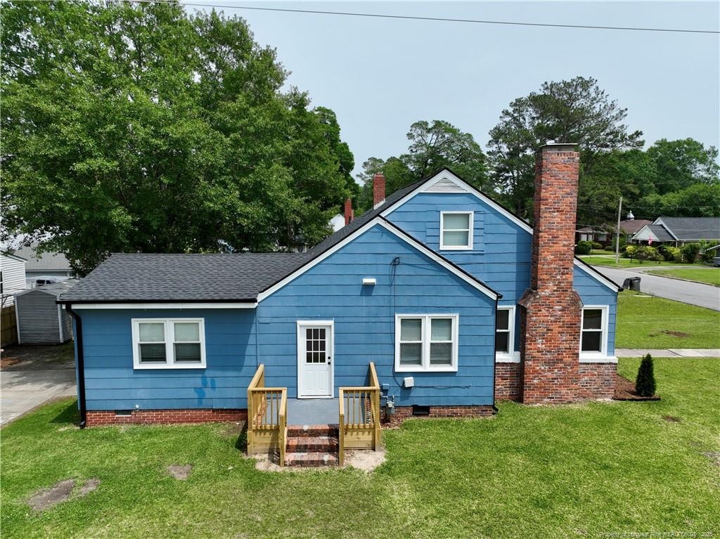 rear view of property with a chimney, a lawn, crawl space, and roof with shingles