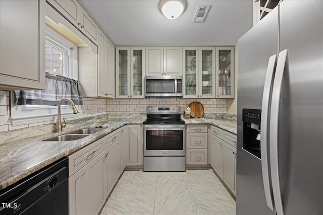 kitchen featuring appliances with stainless steel finishes, a sink, decorative backsplash, and light stone counters