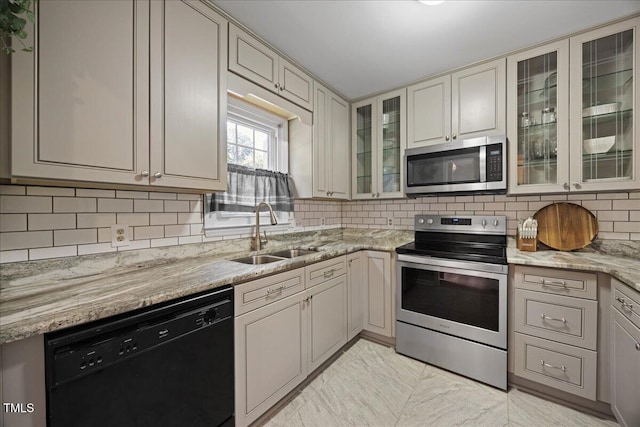 kitchen featuring stainless steel appliances, a sink, decorative backsplash, light stone counters, and glass insert cabinets