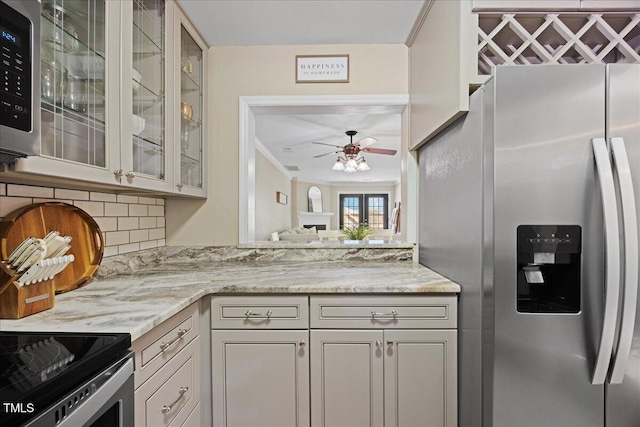 kitchen featuring stainless steel appliances, a ceiling fan, glass insert cabinets, light stone countertops, and decorative backsplash
