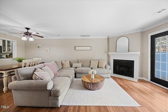 living area featuring wood finished floors, crown molding, a fireplace with flush hearth, a ceiling fan, and baseboards