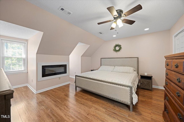 bedroom featuring wood finished floors, a textured ceiling, baseboards, ceiling fan, and lofted ceiling