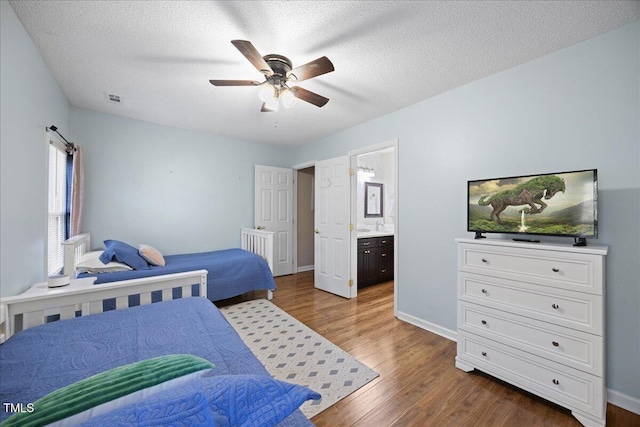bedroom with dark wood finished floors, baseboards, ensuite bath, a ceiling fan, and a textured ceiling