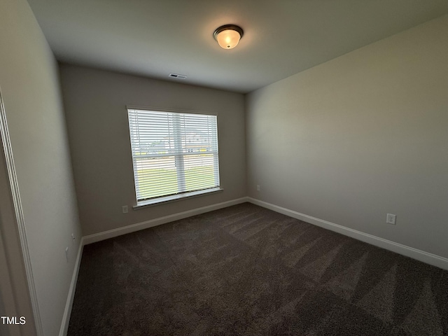 spare room featuring dark carpet and baseboards