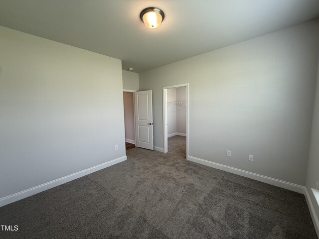 unfurnished bedroom with a spacious closet, carpet flooring, baseboards, and a closet