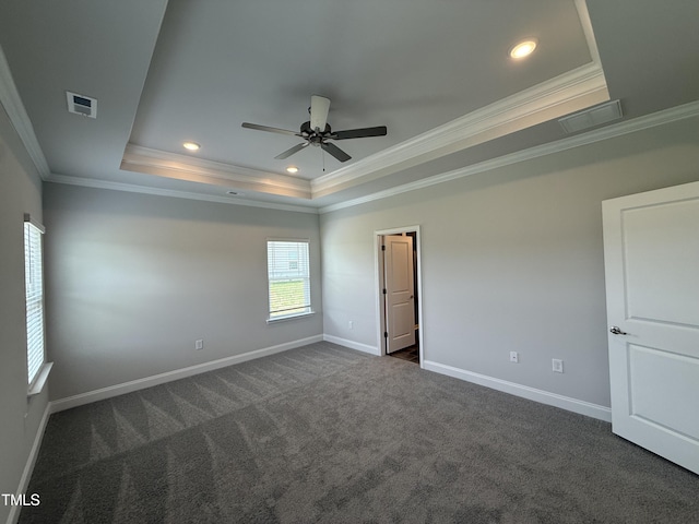 spare room with a tray ceiling, crown molding, dark carpet, baseboards, and a ceiling fan