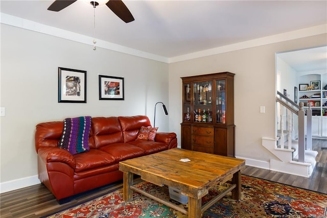 living area featuring wood finished floors, baseboards, ceiling fan, and stairway