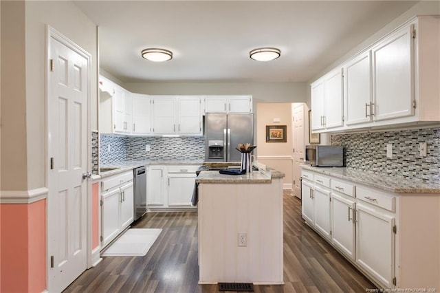kitchen with appliances with stainless steel finishes, decorative backsplash, a center island, dark wood finished floors, and light stone countertops