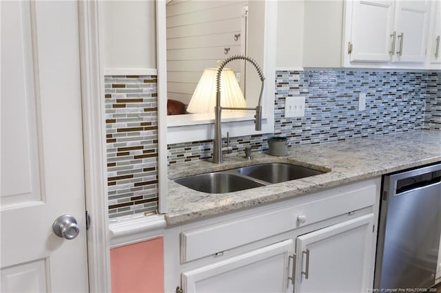 kitchen with stainless steel dishwasher, a sink, tasteful backsplash, white cabinetry, and light stone counters