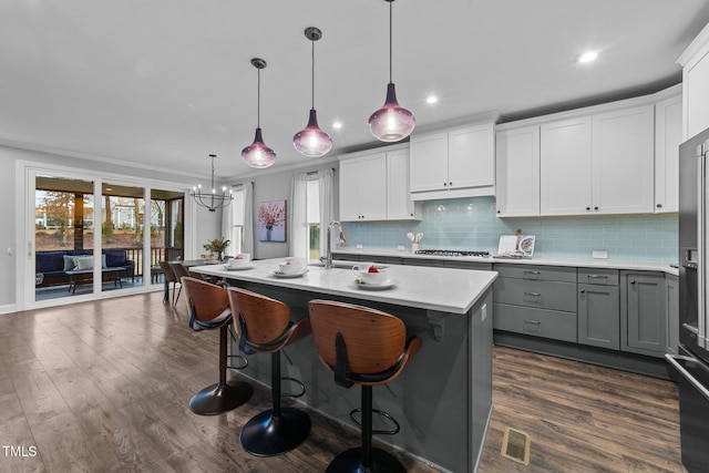 kitchen with gray cabinetry, decorative backsplash, dark wood-style floors, a chandelier, and a sink