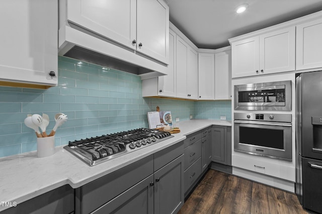 kitchen with stainless steel appliances, gray cabinetry, light stone countertops, white cabinets, and decorative backsplash