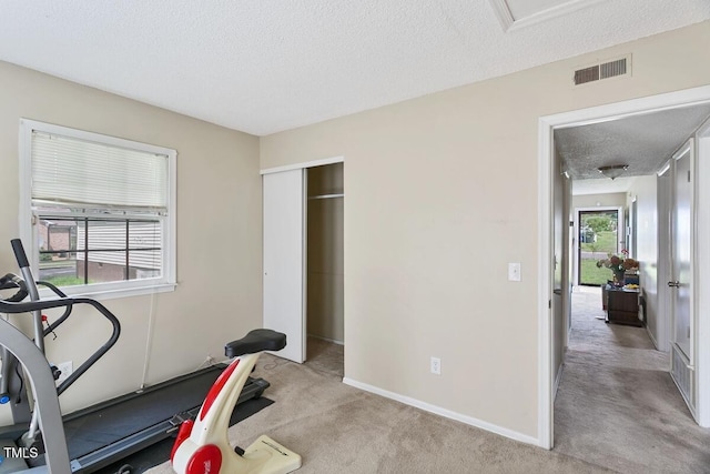 exercise area with a textured ceiling, light colored carpet, and baseboards