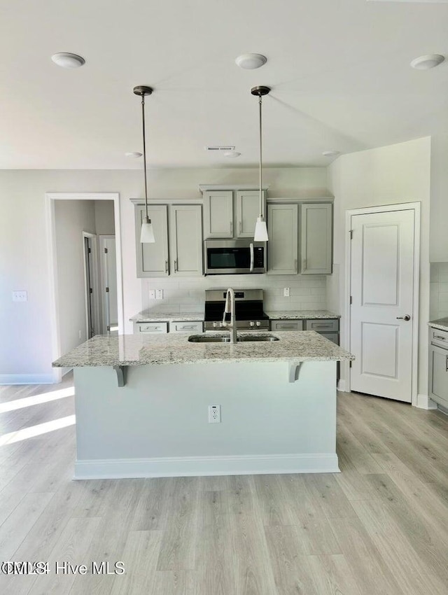 5134 Holly Hill Ct Lot 28, Battleboro, NC 27809 - kitchen featuring stainless steel appliances, a sink, light wood-type flooring, an island with sink, and light stone countertops