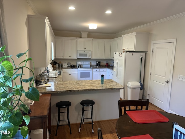 kitchen featuring white appliances, a peninsula, crown molding, wood finished floors, and white cabinets