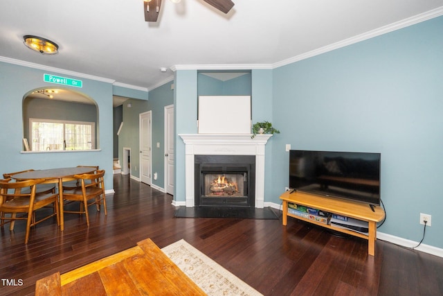 living room featuring crown molding, ceiling fan, a fireplace with flush hearth, wood finished floors, and baseboards