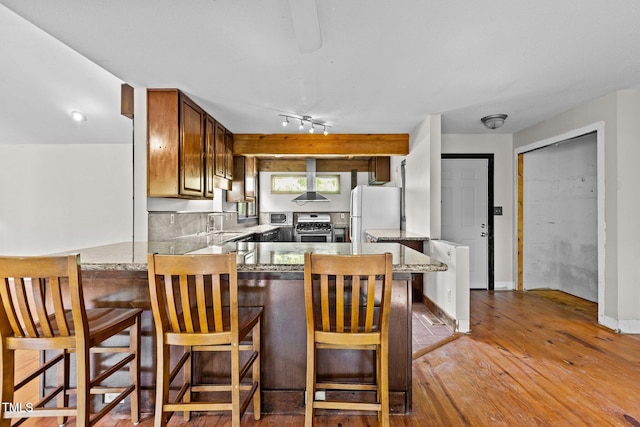 5900 Ebenezer Church Rd, Raleigh, NC 27612 - kitchen with stainless steel range with gas stovetop, freestanding refrigerator, light wood finished floors, a peninsula, and wall chimney range hood